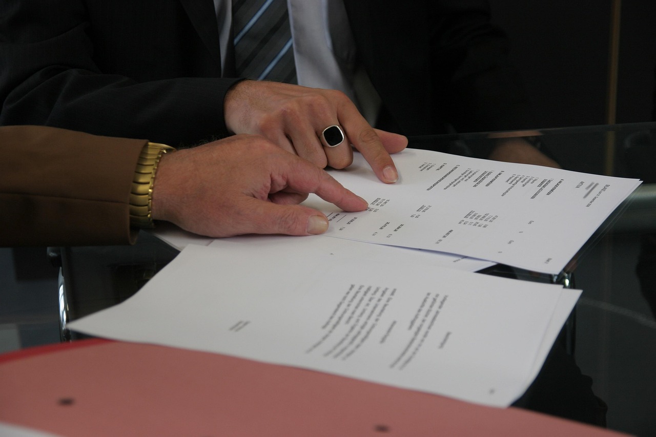Two advisers in businesswear going over printed documents together at a glass desk